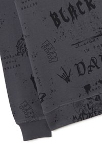 Sudadera gris con estampados gráficos en negro, que incluyen texto, calaveras y patrones. El material es suave con un acabado ligeramente texturizado.