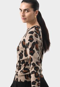 Sweter w leoparda w beżowym kolorze z czarnymi i brązowymi plamami. Posiada okrągły dekolt i ryfledowany dół. Miękka tekstura, dopasowany krój.