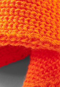 Strikklæde i lys orange garn, med en struktureret, chunky vævning og en fuzzy overflade, med synlige løkker og en blød følelse.