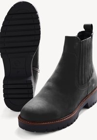 Bottines en cuir noir avec panneaux latéraux élastiques, couture marron décorative et semelles en caoutchouc rainurées, vues de côté et de dessous.