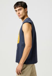 Marinblå ärmlös bomullströja med ett gult grafiskt mönster; rak passform och en mjuk textur; synlig sömnad vid ärmhål och fåll.