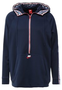 Marinblå zip-up hoodie tillverkad av slät tyg; har ett mönstrat foder i huven, röd dragkedja, ficka framtill och en liten logotyp på bröstet.