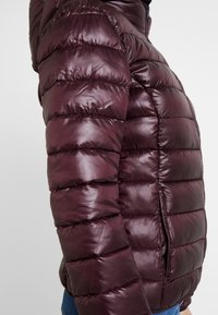 Burgundy puffer jacket with a glossy finish, featuring horizontal quilted segments, a hood, and side zipper pockets.
