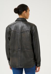 Zwarte leren jas met een gestructureerde pasvorm, zichtbare stikdetails en een klassieke kraag. Glad oppervlak met een lichte glans en knopenmanchetten.