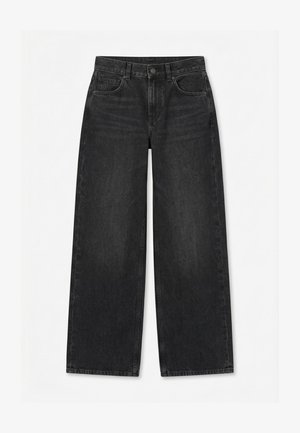 Melnas platām kājām džinsi ar priekšpuses pogu un rāvējslēdzēju, jostas cilpām un piecu kabatu dizainu uz vienkrāsaina balta fona.