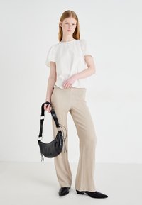 Hvit bluse med puffermer, beige plissert bukser, svart strukturert veske med flettet stropp, og spisse svarte hæler mot en nøytral bakgrunn.