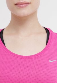 Rosa, ärmlös träningslinne med rund halsringning och ett texturerat, ventilerande tyg. Har en liten silverfärgad Nike-logotyp på övre högra sidan.