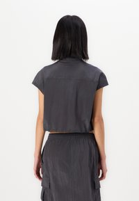 Donkergrijze cropped top met korte mouwen, casual stof en een iets rafelige zoom, gedragen met een bijpassende rok met trekkoord in de taille.
