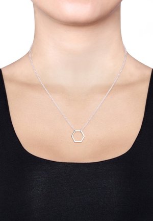 Silberne Halskette mit einem Sechseck-Anhänger, ausgestattet mit einer filigranen Kette und einem minimalistischen Design, getragen auf einem nackten Hals über einem schwarzen Oberteil.