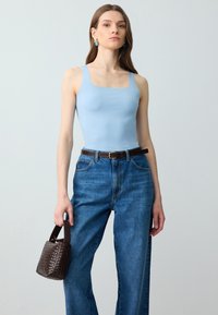 Top in cotone azzurro fitted, jeans in denim blu a vita alta, borsa intrecciata scura, design minimalista, tessuto morbido, illuminazione naturale.