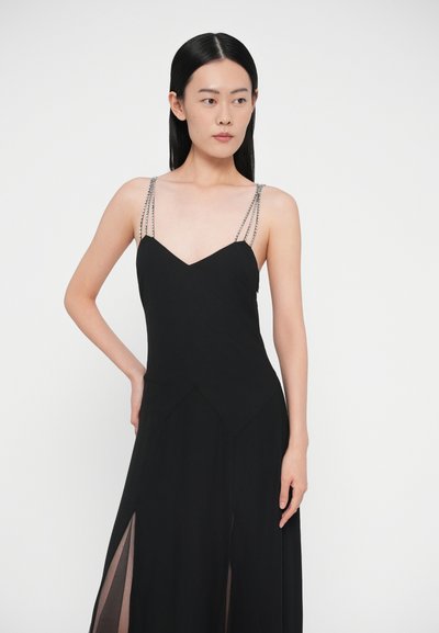 Rochie neagră cu corset strâmt, decolteu în V și panouri laterale transparente. Prezintă bretele cu mărgele argintii și o siluetă în formă de A. Textură moale.