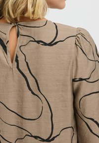 Beige Bluse mit schwarzen abstrakten Linienmustern, einem Schlüsselloch-Ausschnitt auf der Rückseite und Puffärmeln aus leichtem Stoff.