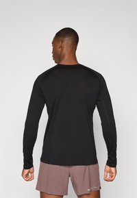 Schwarzes Langarmshirt mit rundem Ausschnitt und Raglanärmeln, kombiniert mit rosa Shorts. Der Stoff wirkt leicht und glatt.
