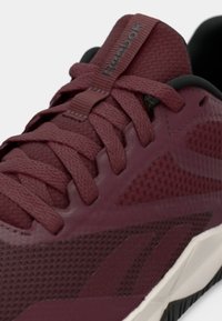 Reebok bordó sportcipő, háló- és szintetikus anyagokkal, hat strapabíró fűzővel, texturált díszítésekkel és fehér középtalppal.