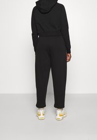 Black cropped hoodie with a hood, paired with high-waisted black sweatpants. Sneakers feature white, yellow, and gray accents.