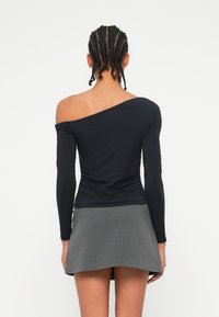 Crna majica bez naramenica s dugim rukavima, s nabranim detaljima na leđima, u kombinaciji s sivom mini suknjom s izrezima.