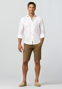 Chemise en lin blanc léger avec un col boutonné, assortie à un short beige et des espadrilles beiges. Coupé simple et décontracté.
