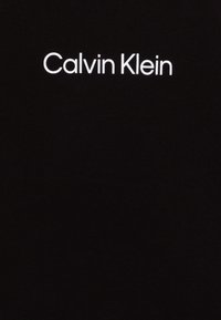 Zwarte stof met de tekst "Calvin Klein" in witte, schreefloze lettertype, centraal gepositioneerd. Minimalistisch ontwerp zonder extra details.