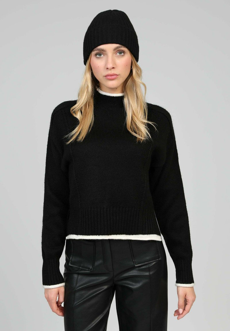 Pull en tricot noir à col montant et ourlet blanc, associé à un pantalon en cuir noir et un bonnet côtelé assorti, avec des manches longues.