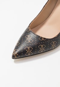 Pompe noire à talons pointus, fabriquée en matériau synthétique texturé, avec un motif de logo beige et un intérieur lisse beige.