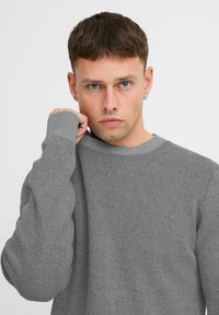 Maglione grigio a texture con scollo rotondo e polsini a costine, caratterizzato da una vestibilità ampia e da un sottile motivo a nido d'ape su tutta la stoffa.