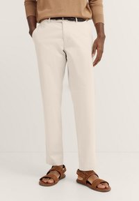 Beige Hose mit geradem Bein, aus Baumwollmaterial, mit Seitentaschen, kombiniert mit braunen Sandalen mit verstellbaren Riemen.