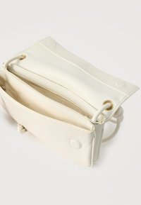 Μικρή κρεμ δερμάτινη τσάντα χιαστί με ανοιχτό καπάκι, που δείχνει το εσωτερικό διαμέρισμα με φερμουάρ και μαγνητικά κλείστρα.