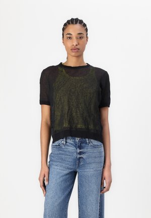 Svart, gjennomsiktig topp med kort erme og scoop-hals, lagd over en grønn tanktopp. Kombinert med lyseblå, vide jeans med falmede detaljer.