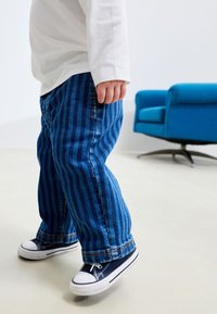 Blå randiga jeansbyxor med avslappnad passform, kombinerade med marinblå canvas-sneakers med vita gummisulor. Enkel vit långärmad tröja.