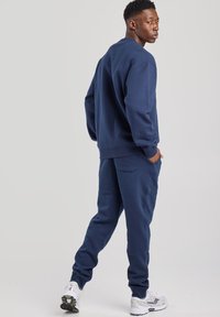 Navy blue sweatshirt and sweatpants set in soft fabric. Crew neck design, elastic cuffs, and pockets in pants. Athletic white sneakers.