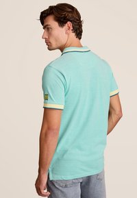 Polo shirt in muntgroene katoen, met een klassieke kraag, gele en marineblauwe gestreepte manchetten en een logo patch op de linkermouw.