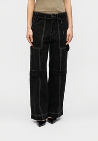 Μαύρο παντελόνι cargo με χαλαρή εφαρμογή, με λευκή ραφή, πολλαπλές τσέπες και ελαστική μέση με κορδόνι. Το ύφασμα έχει ανθεκτική υφή.