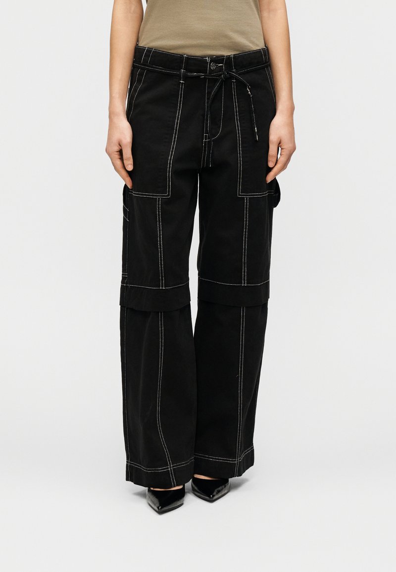 Μαύρο παντελόνι cargo με χαλαρή εφαρμογή, με λευκή ραφή, πολλαπλές τσέπες και ελαστική μέση με κορδόνι. Το ύφασμα έχει ανθεκτική υφή.