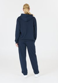 Conjunto de sudadera con capucha y pantalones en azul marino, fabricado en tejido suave, con capucha, puños acanalados y un corte relajado. Diseño sencillo sin patrones visibles.