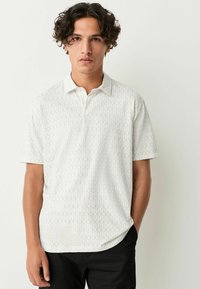 Balta trumpomis rankovėmis polo marškinėliai su geometriniu raštu. Savybės: apykaklė ir laisvas siluetas, pagaminti iš lengvos medžiagos.