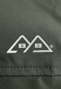 Donkergroene stof met een zilveren logo dat twee driehoeken en de tekst "BB" in het midden bevat, gelegen nabij een gestikte naad.