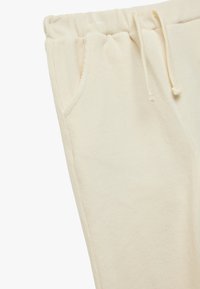 Pantalon de survêtement crème avec taille élastique, cordon de serrage et poches latérales. Confectionné en tissu doux avec une texture côtelée.