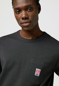 Zwarte pocket t-shirt van katoen. Beschikt over een borstzak met een kleurrijk Wrangler-logo. Ronde halslijn en gestructureerde stof.