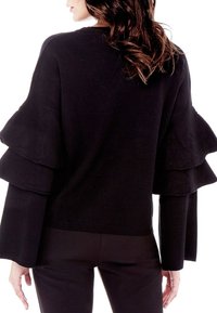 Schwarzer Pullover mit gerüschten Glockenärmeln, strukturiertem Stoff, Rundhalsausschnitt und angepasstem Schnitt, getragen mit Slim-Fit-Hosen.