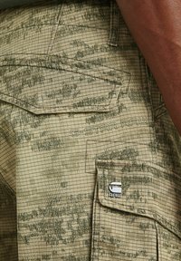 Beige cargobroek met een ruitpatroon en groene accenten, voorzien van utilityzakken en een G-Star RAW-logo gestikt aan de zijkant.