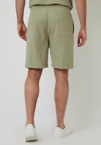 Groene heren shorts van textuurstof, met een achterzak en een rechte snit, gecombineerd met witte sneakers.