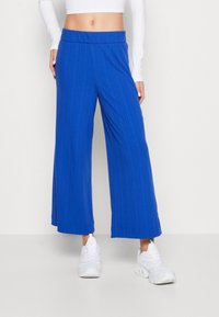 Pantalons larges à côtes bleues avec une taille élastique, présentant une texture lisse et une coupe décontractée, associés à des baskets blanches.