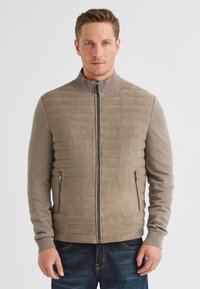 Beige Zip-Jacke mit Reißverschluss, geripptem Kragen, gestepptem Körper und langen Ärmeln. Verfügt über Seitentaschen und eine glatte, weiche Textur.