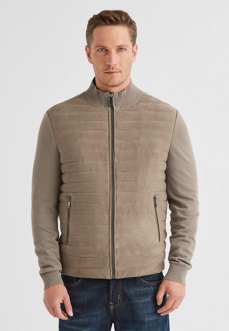 Beige Zip-Jacke mit Reißverschluss, geripptem Kragen, gestepptem Körper und langen Ärmeln. Verfügt über Seitentaschen und eine glatte, weiche Textur.