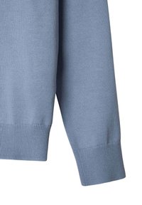 Manica di un pullover lavorato a maglia di colore blu chiaro con polsini a costine, che mostra una texture liscia e cuciture uniformi. Nessun logo o motivo visibile.