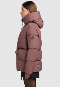 Chaqueta acolchada en malva con un cuello alto, cordones ajustables, puños elásticos y un parche con logo en la manga. Tejido texturizado.