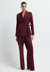 Bordeaux maatpak set met een wikkelblazer met een strik taille en bijpassende wijde pantalons. Gladde stof met een matte afwerking.