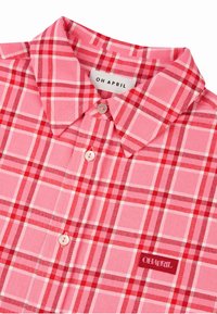 Koszula w kratę w różowo-czerwonych odcieniach, z kołnierzykiem w szpic, zapięciami na guziki oraz metką z napisem "OH APRIL." Miękka tekstura tkaniny.