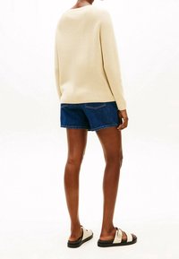 Pull beige en maille, short en denim bleu et sandales blanches avec une semelle noire. Le pull a une coupe décontractée et une texture côtelée.