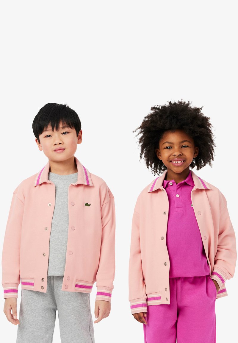 Růžové bavlněné bomberové bundy s pruhovanými žebrovanými manžetami a límci. Zelené logo na levé hrudi. Šedé a růžové spodní vrstvy.